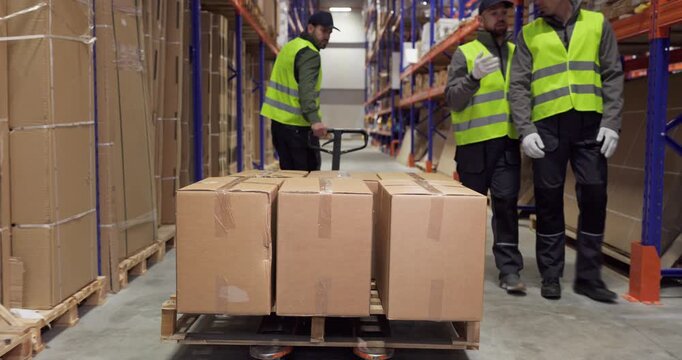 Worker warehouse pallet truck loading boxes delivery. Two coworkers in safety vests manage cargo near shelves, keeping logistics smooth and inventory ready for shipping. Team at work keeps flow.
