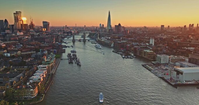 England, London skyline at sunset, River Thames winding past Tower Bridge and The Shard, blending historic landmarks and modern urban cityscape architecture in golden evening glow. Aerial view flight