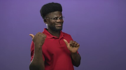 Man wearing glasses gives thumbs up and points thumb to chest in studio with purple wall; confidence approval.