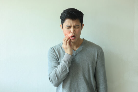 close up young asian man frown and use hand to massage on cheek after feeling pain or hurt from tmj muscle symptom at home for un healthy lifestyle and treatment concept