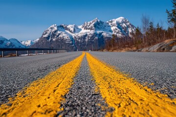 Scenic Road Leading to Snow Capped Mountains Under Blue Sky on Sunny Day Asphalt Road with Yellow Lines Provides Perspective and Depth