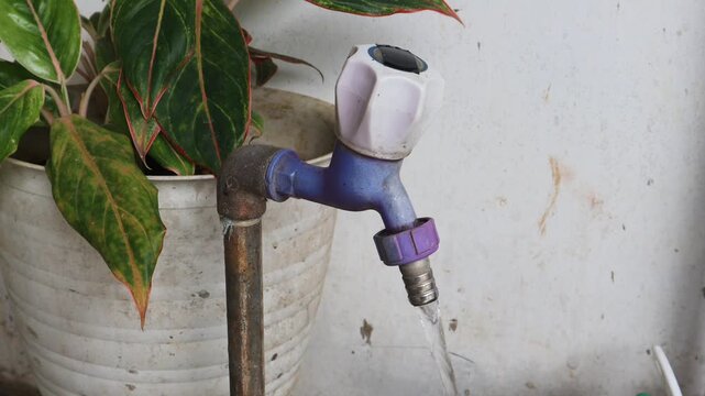 Water tap for watering a garden plot outside the house. Water is pouring out of tap. Man turns off the valve and cut off the water. 