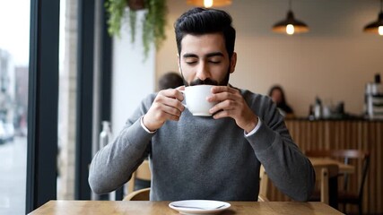 Young Man Enjoying a Relaxing Coffee Break in a Cozy Cafe, Looking Thoughtful and Content.