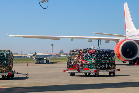 Airport Baggage and Cargo Loading Under Airplane Wing. 
Airport ground handling scene showing baggage and cargo containers loaded onto carts beneath a commercial airplane wing on the runway. 