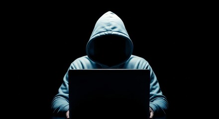 Person in hoodie using laptop in dark environment for anonymous online activity or cyber security concept