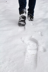 Vertical winter photo of male legs in boots stepping into pristine snow. Copy space, minimal composition