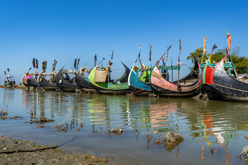 Obraz premium Traditional Moon Boat (Sampan) Beached on the Shores of Teknaf, Cox's Bazar. Colorful Wooden Fishing Boat on a Sandy Beach under Clear Blue Sky in Bangladesh. Vibrant Traditional Fishing Vessel on the