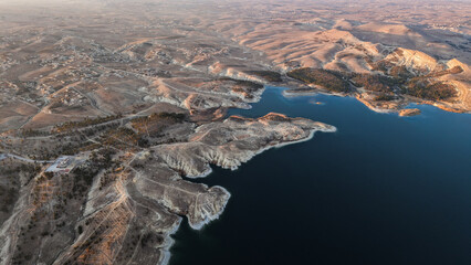 Tishrin Dam in Syria. A massive water dam in the desert. High-angle drone shot showing a giant dam structure holding back turquoise river water amid an arid desert landscape, used for water management