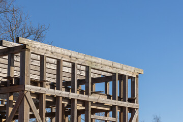 Timber frame construction rises with wooden scaffolding under a bright blue sky