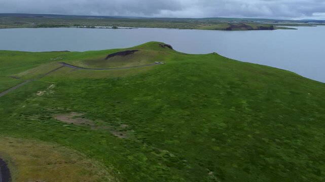 Aerial drone pan of Lake Myvatn with green volcanic pseudo craters and calm water. Wide landscape shows unique geology and remote natural beauty of northern Iceland.