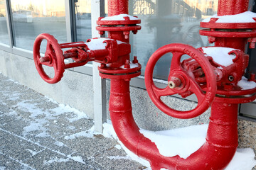 Red industrial gas pipes with valves covered in snow outdoors