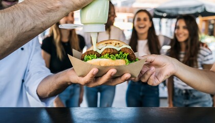 Slightly cropped hands of a Chef squeezing green sauce onto a vegetable patty burger served to a customer outdoors, concept for quick service promotion, food truck menu and casual dining marketing