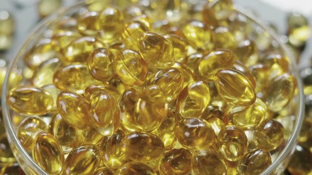 Close-up video of golden softgel capsules in lab glass plate, rotating slowly and this shows concepts related to biotechnology, science, healthcare, nutritional supplements, and daily wellness.