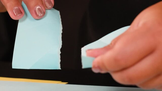 Close Up View of Hands Tearing Light Blue Paper Into Small Pieces