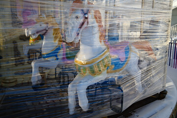 Carousel horse wrapped in protective plastic, amusement park off season, winter storage of fairground ride
