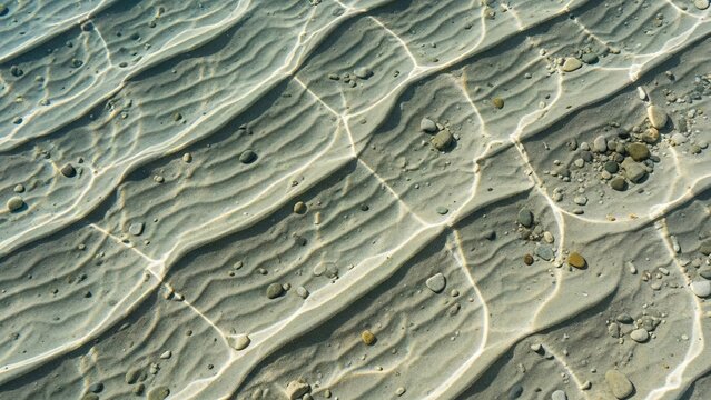 Rippled sand under clear water with pebbles creating an underwater scene