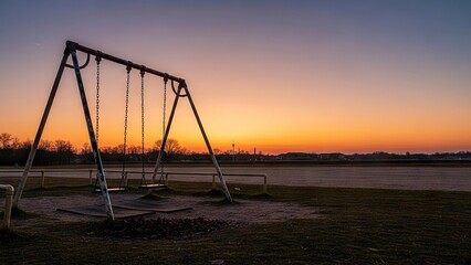 Fototapeta premium A metal swing set stands in a parklike setting at sunrisesunset