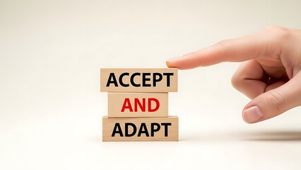 Human hand pointing to a stack of wooden blocks spelling 'ACCEPT AND ADAPT' on a clean white background, emphasizing resilience and change.