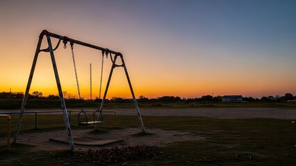 A weathered swing set stands silhouetted against a vibrant gradient sunset sky