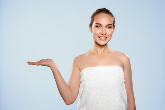 Woman in white towel shows hand gesture against light blue background