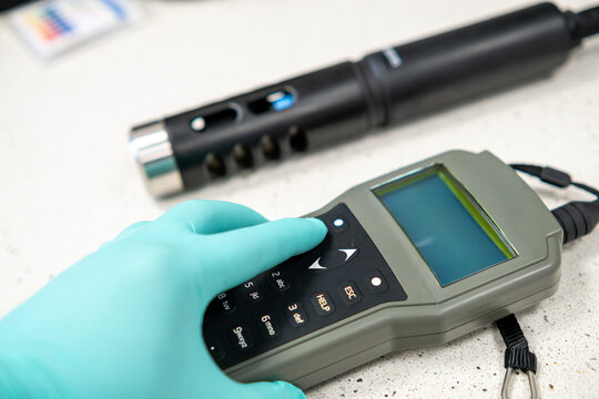 Close up of gloved hands pressing buttons on a portable pH meter during measurement.