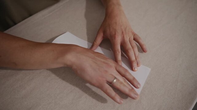 Medium top-down shot showing an adult man carefully folding a paper airplane on a table. Camera captures calm movements and step-by-step paper folding. High quality 4k footage