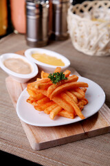 Crispy seasoned French fries served on a white plate with dipping sauces, garnished with parsley on a wooden board. Close up food photography, warm lighting, perfect for restaurant menu, snack concept