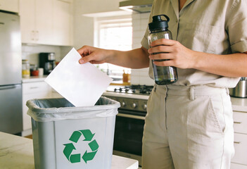 Hand putting paper into a grey recycling bin with green symbol