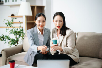 Asian businesswomen collaborating on laptop and tablet in modern office. Professional teamwork, startup meeting, planning, consulting