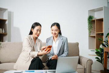 Happy Asian businesswomen celebrating success together at office. Teamwork, collaboration, business achievement, financial growth and positive corporate work concept.