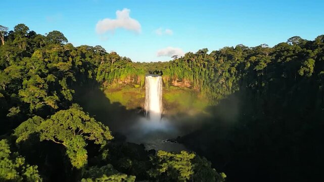 Majestic waterfall cascades down jungle-covered cliffs under a bright blue sky