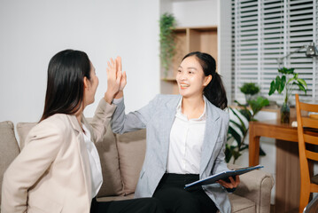 Happy Asian businesswomen celebrating success together at office. Teamwork, collaboration, business achievement, financial growth and positive corporate work concept.