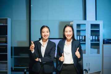 Confident Asian businesswomen smiling and showing thumbs up in modern office. Professional teamwork, success, trust, leadership