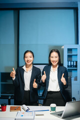 Confident Asian businesswomen smiling and showing thumbs up in modern office. Professional teamwork, success, trust, leadership