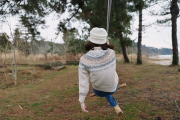 Swing, outdoor forest scene with a person in a cozy sweater and beanie, enjoying autumn calm on a simple swing amid trees, nature and solitude.
