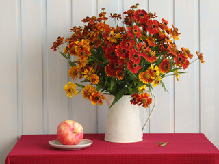 Autumn helenium flowers with apple on red tablecloth
