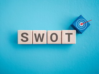 Wooden blocks displaying SWOT letters with target icon symbolizing goal, strategy and perform analysis on blue background. Ideal for business planning and consulting visual.
