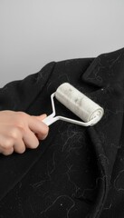 Removing Hair From Black Coat With Roller. Hand holding cleaning tool to sticky dust and fluff from fabric jacket. Laundry care removing pet fur dander from textile garment for neat look.