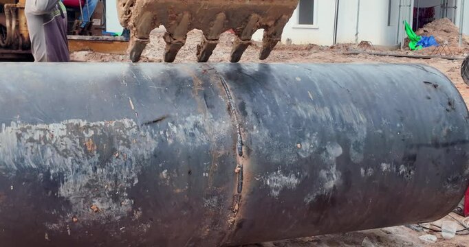 close up of an excavator bucket positioning a large metal piling casing at a construction site.
