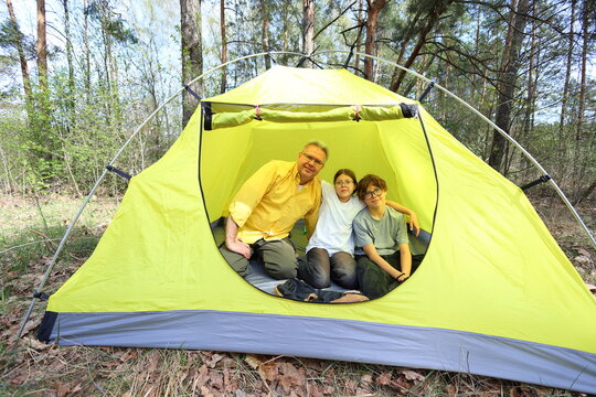 A father hugs his two kids inside a bright yellow tent in the forest. A warm, joyful snapshot of family love, comfort, and adventure on a sunny camping day.