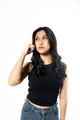 Fototapeta premium Thoughtful Asian woman in black tank top looking up and touching temple with finger, isolated on white background, dreaming or making a decision