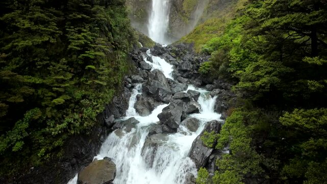 View up waterfall from rocky cascades in lush green gorge