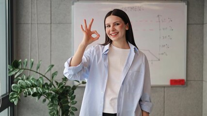 Professional woman expresses confidence with okay sign. Positive gesture conveys happiness, success. Demonstrates approval for business achievements.