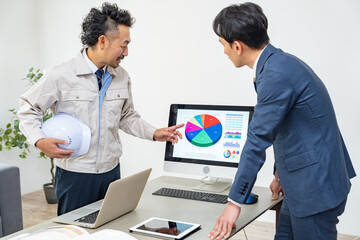 打ち合わせをする作業着、スーツを男性たち