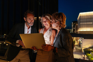 Businesspeople working late at night using laptop on rooftop