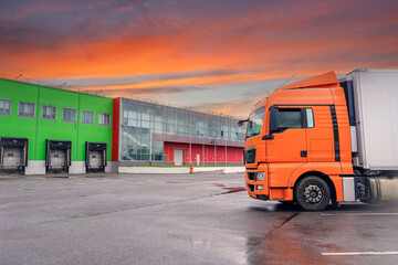 Big truck with orange cab at dawn with beautiful sky in parking lot of warehouse storage waiting to be loaded at gate