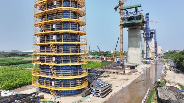 Construction site of elevated bridge piers with yellow formwork tower and crane operation