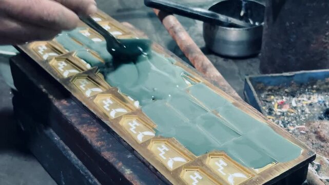 Close-up view of a craftsman carefully filling a decorative mold with liquid resin or enamel using a spatula. The image highlights skilled handwork, traditional craftsmanship