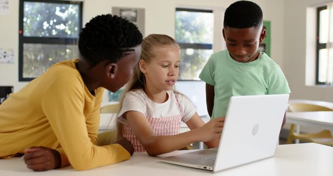 Diverse children gathering around laptop at school, girl leading, typing and pointing at screen