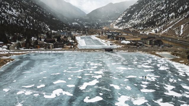 Aerial View of Two People on a Frozen Lake in a Mountain Valley